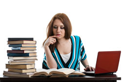 Our editors explain how to create a bibliography using word. A red haired student is sitting with a stack of books and a laptop; she is learning how to create her bibliography using word.