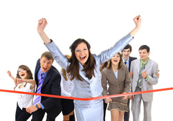 A woman in a business suit is crossing the finish line because she just won a short story contest. There are seven people in business attire close behind her.