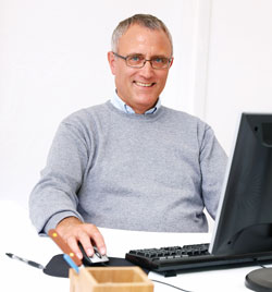 An older man is dressed casually and sitting down at a computer. He is looking at the new Scribendi.com 2.0 website.
