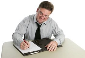 A male professor is sitting at a desk with a clipboard in front of him. He is poised for writing and is beginning the first steps of grant writing.