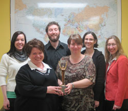 The Scribendi.com staff stand in front of a large map of the world while holding their International Stevie Award for Best Writing/Content.