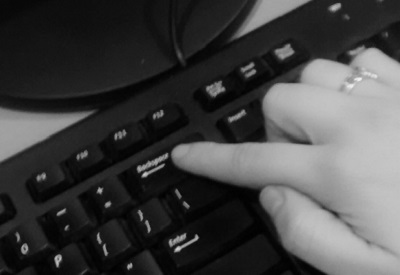 A hand presses the backspace button on a keyboard.