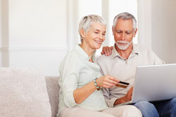 An elderly couple are sitting on a couch and placing an order on the Scribendi.com website by using the Discover Card payment option. 