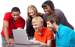 Five students dressed in casual attire are standing around a computer looking at the English Idioms website What Does That Mean?