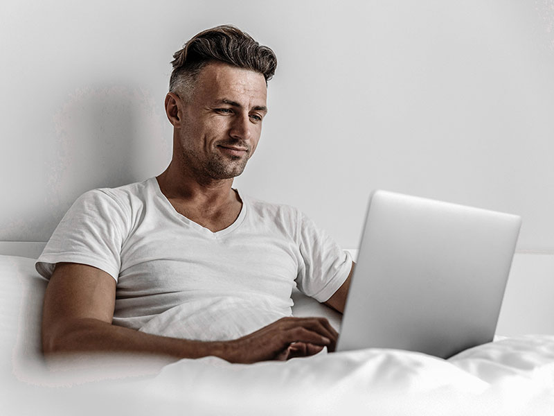 A man working on his laptop in bed.